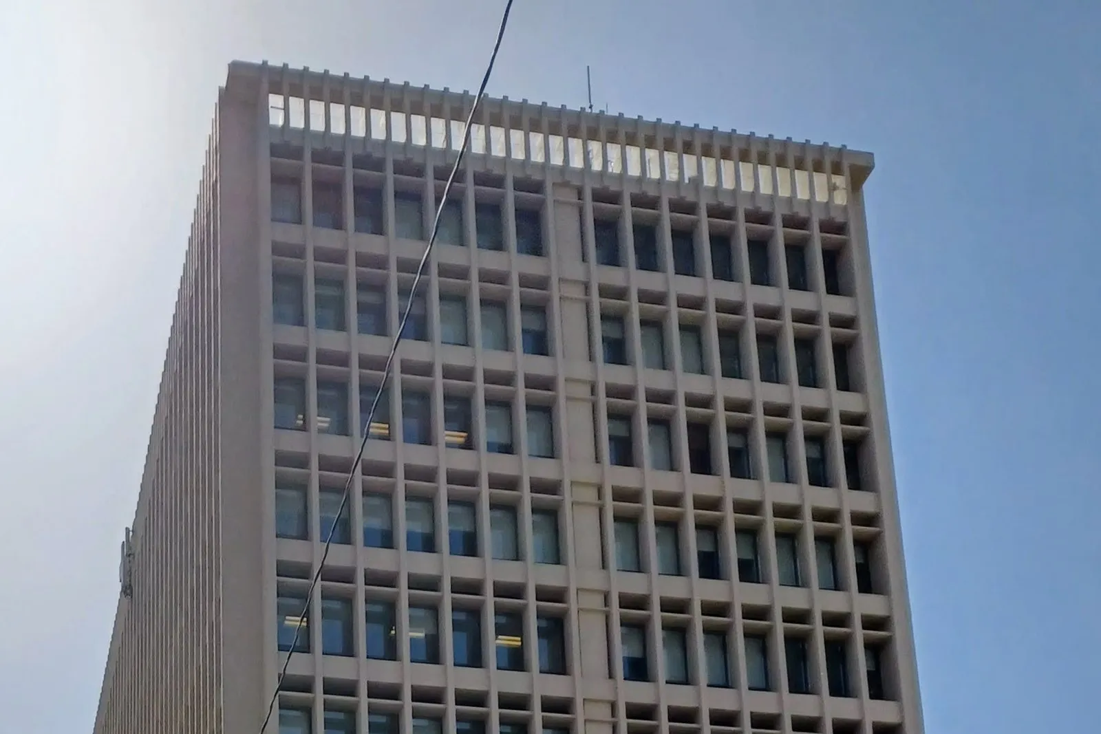 The upper floors of the PNM Building in Albuquerque, a pale concrete tower with a grid of recessed windows, seen from below against a blue sky