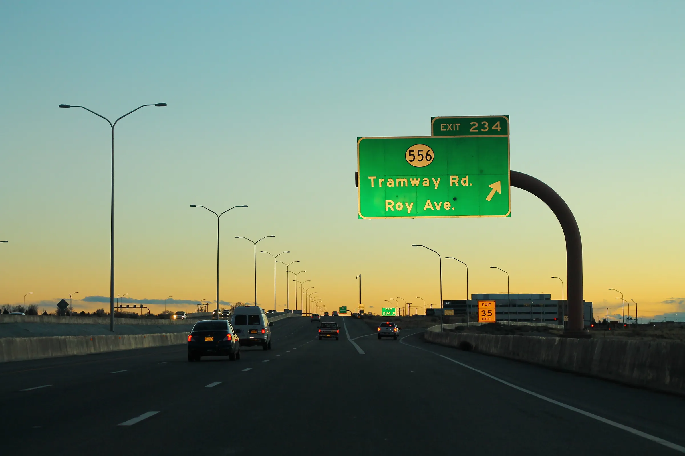 Cars on southbound Interstate 25 at dusk, under an overhead green sign for Exit 234, Tramway Road and Roy Avenue